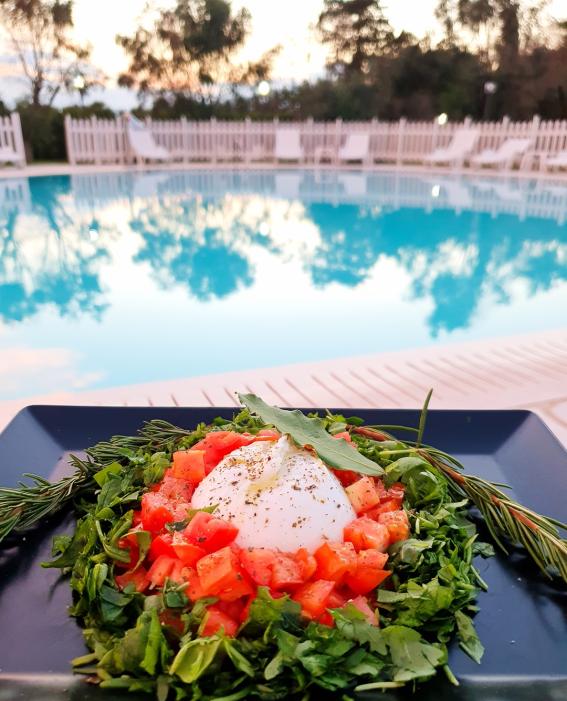 Burrata dish with tomatoes and greens, near a pool.
